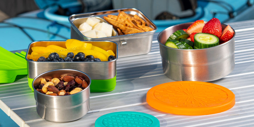 Four Blue Water Bento stainless steel food containers holding fruits, nuts, and more healthy snacks.