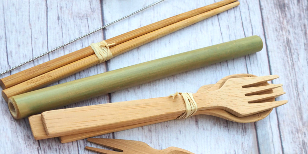 Bamboo fork, spoon, straw, and chopsticks on a wooden table.